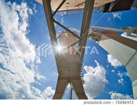 White cargo crane in the harbour, photographed from below in the direction of the sun through the supports, abstract impression, industry White cargo crane in the harbour, photographed from below in the direction of the sun through the supports, abstract impression, industry 78896455