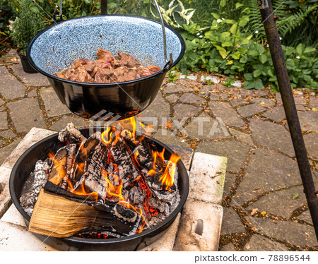 Frying the beef in a cauldron over an open wood fire to prepare the Hungarian cauldron goulash, food 78896544