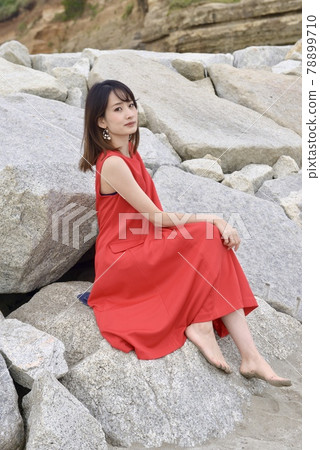 一位身穿紅色連衣裙的年輕女子坐在落基山上微笑 78899710