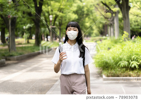 A girl walking in the park wearing a mask and holding a plastic bottle in midsummer 78903078