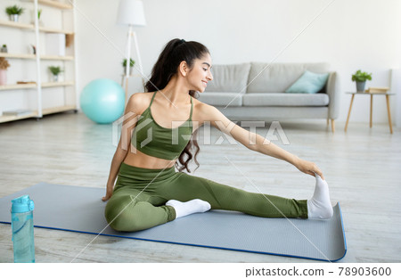 Young Indian lady stretching on yoga mat, making domestic workout, doing flexibility exercises at home 78903600