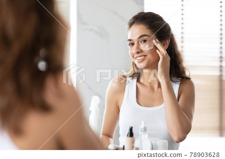 Attractive Female Applying Cream Moisturizer On Skin In Bathroom Indoors Attractive Female Applying Cream Moisturizer On Skin In Bathroom Indoors 78903628