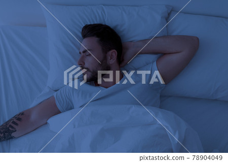 Young man sleeping peacefully at night, lying with closed eyes in comfortable bed in bedroom at home. 78904049