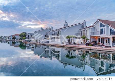 Houses along border of mirror like sea with water that reflects the cloudy sky 78905917