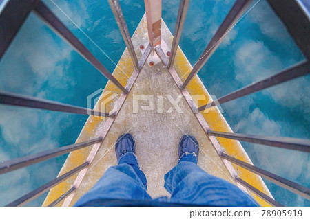 Man standing on the corner of deck against harbor water with reflection of sky 78905919