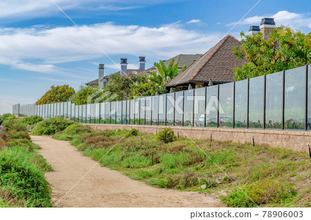 Narrow pathway in front of homes under cloudy blue sky in a seaside neighborhood 78906003