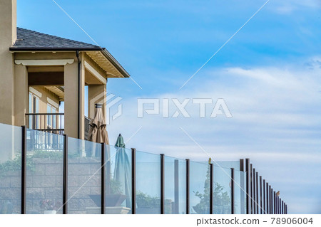 House exterior with balcony and glass fence against cloudy blue sky background House exterior with balcony and glass fence against cloudy blue sky background 78906004