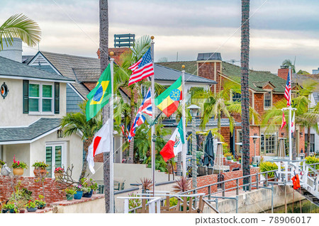 Waterfront houses colorful flags and palm trees along a canal under cloudy sky Waterfront houses colorful flags and palm trees along a canal under cloudy sky 78906017