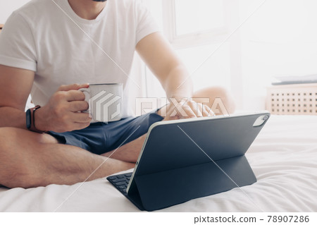Man work with tablet and coffee in bedroom. Concept of work from home. Man work with tablet and coffee in bedroom. Concept of work from home. 78907286