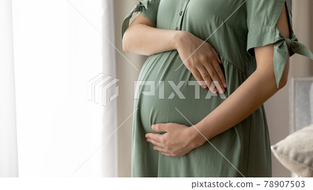 Close up cropped of pregnant woman in dress embracing belly 78907503
