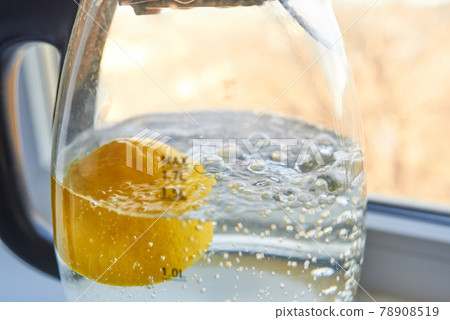 Half a yellow lemon is boiled in a glass electric kettle for descaling 78908519