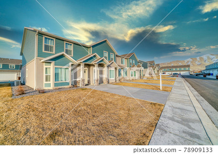 Townhouses with teal wooden wall against snowy mountain and cloudy sky 78909133