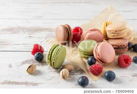 Variety of french macaroons with berries such as raspberry and blueberry over wooden background. 78909408