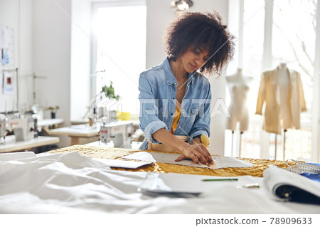 African-American seamstress works with sewing patterns and yellow fabric at cutting table African-American seamstress works with sewing patterns and yellow fabric at cutting table 78909633