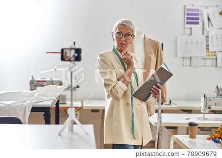 Serious mature fashion designer looks at camera shooting video for blog in workshop 78909679