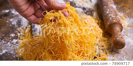 Italian egg pasta, homemade and fresh on a wooden table. Tagliatelle pasta is thin. In hand Italian egg pasta, homemade and fresh on a wooden table. Tagliatelle pasta is thin. In hand 78909717