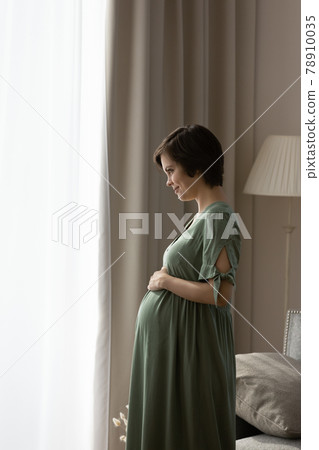Vertical photo of profile pregnant woman in dress touching belly 78910035