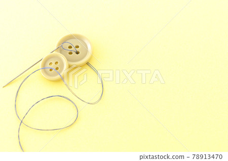 Shooting buttons, needles and threads on a light yellow background 78913470