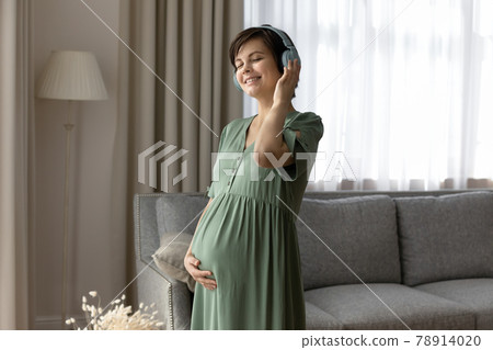 Smiling pregnant woman in headphones enjoying favorite music, touching belly 78914020