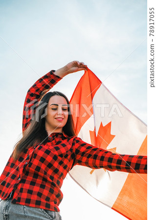 Young millennial brunette woman holding The National Flag of Canada. Canadian Flag or the Maple Leaf. Tourist traveler or patriotism. Immigrant in a free country. Independence day 1th july 78917055