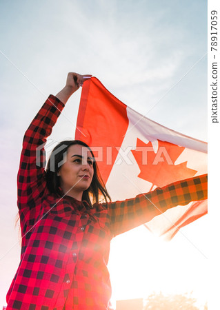 Young millennial brunette woman holding The National Flag of Canada. Canadian Flag or the Maple Leaf. Tourist traveler or patriotism. Immigrant in a free country. Independence day 1th july Young millennial brunette woman holding The National Flag of Canada. Canadian Flag or the Maple Leaf. Tourist traveler or patriotism. Immigrant in a free country. Independence day 1th july 78917059