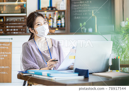 A woman working in a cafe-style office wearing a mask 78917544