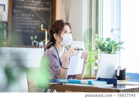 A woman working in a cafe-style office wearing a mask 78917545