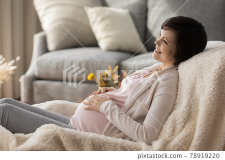 Dreamy smiling pregnant woman touching belly, relaxing in cozy chair 78919220
