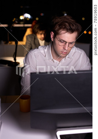 Man realising amount of work in office at night, sitting at desk working on computer 78919603