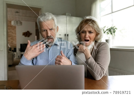 Unhappy old couple shocked by bad news on laptop 78919721