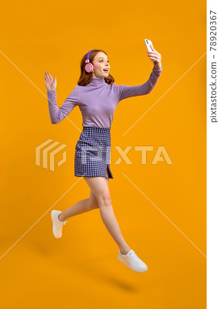 Excited Redhead Woman In Heaphones Jumping, Walking And Talking On Phone Excited Redhead Woman In Heaphones Jumping, Walking And Talking On Phone 78920367