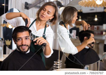 female professional shaving cheerful male's hair 78920787