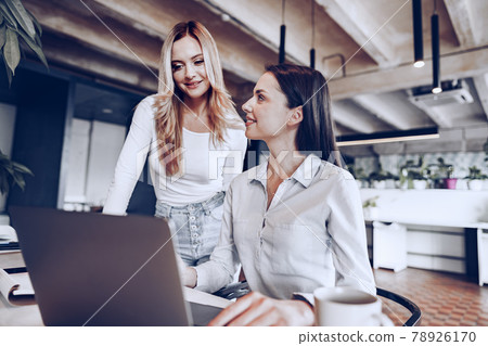 Two young female colleagues discussing business project together in office Two young female colleagues discussing business project together in office 78926170