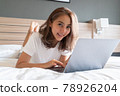 Asian woman lying down and smiling the bed and laptop 78926204