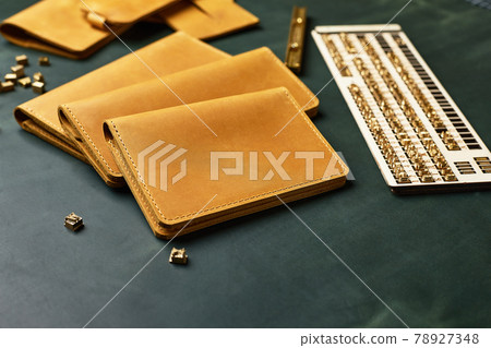 A set of wallets, business card holders and key holders made of handmade leather, yellow with a piece of green leather surrounded by tools, demonstration of handmade leather products 78927348