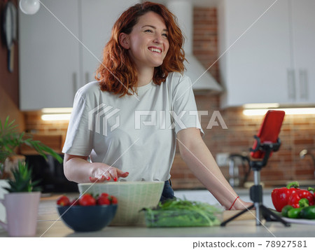 Young pretty woman blogger shoots a video of a salad recipe on a smartphone camera. 78927581