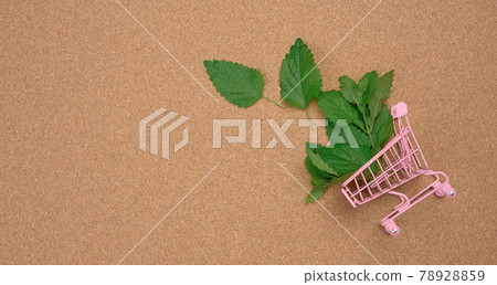 pink miniature metal cart with green mint leaves on brown background pink miniature metal cart with green mint leaves on brown background 78928859