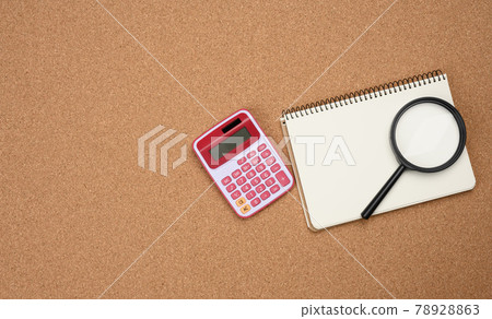 pink calculator, notebook with blank white sheets and black magnifier on a brown background pink calculator, notebook with blank white sheets and black magnifier on a brown background 78928863