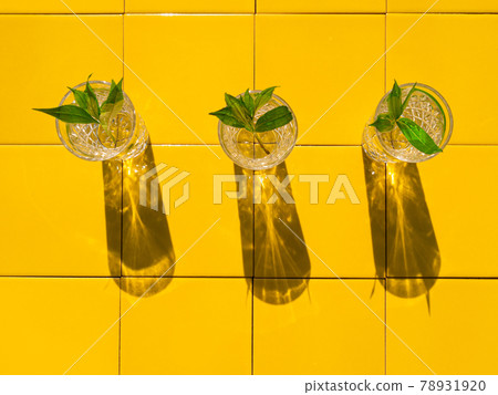 Refreshing summer drinks in crystal glasses with green leaves yellow tile background harsh shadows cold natural cocktail Refreshing summer drinks in crystal glasses with green leaves yellow tile background harsh shadows cold natural cocktail 78931920