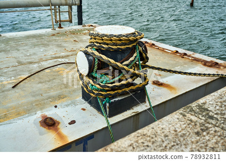 Side view of a cruciform bollard with mooring rope for securing a boat Side view of a cruciform bollard with mooring rope for securing a boat 78932811