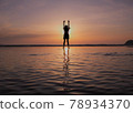 A girl taking a deep breath in front of the setting sun with her hands raised 78934370