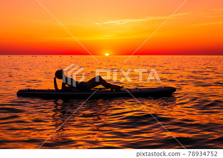 Girl on stand up paddle board at quiet sea with bright sunset or sunrise. Woman relax on sup board in sea. Girl on stand up paddle board at quiet sea with bright sunset or sunrise. Woman relax on sup board in sea. 78934752