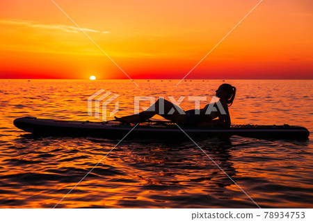 Girl on stand up paddle board at quiet sea with bright sunset or sunrise. Woman relax on sup board in sea. 78934753