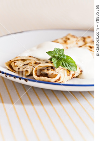 thin crepes rolled pancakes with sour cream mint on a plate 78935569