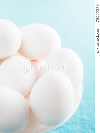 White chicken eggs in a white bowl on a blue background 78935570