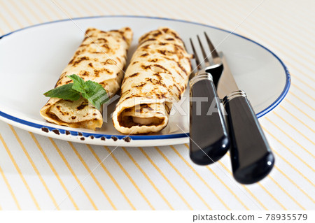 thin pancakes rolled crepes mint on a plate with knife and fork 78935579