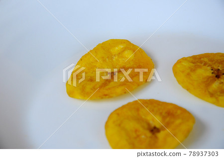 Dried and fried banana slices place on white plate isolated on wood texture background. This is local Malaysian traditional junk food call Kerepek Pisang.    Dried and fried banana slices place on white plate isolated on wood texture background. This is local Malaysian traditional junk food call Kerepek Pisang.    78937303