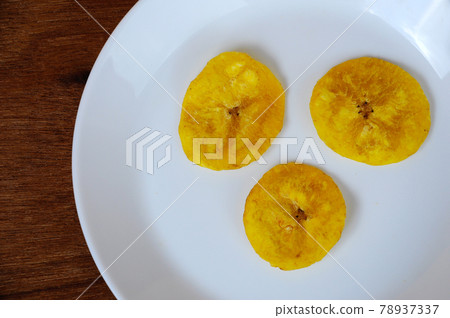 Dried and fried banana slices place on white plate isolated on wood texture background. This is local Malaysian traditional junk food call Kerepek Pisang.    78937337
