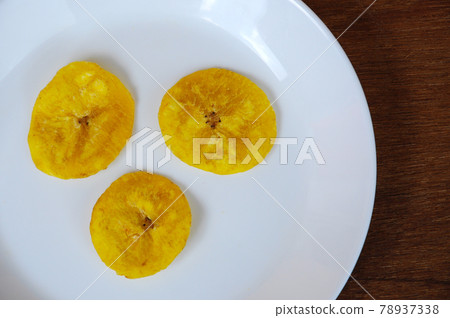 Dried and fried banana slices place on white plate isolated on wood texture background. This is local Malaysian traditional junk food call Kerepek Pisang.    78937338