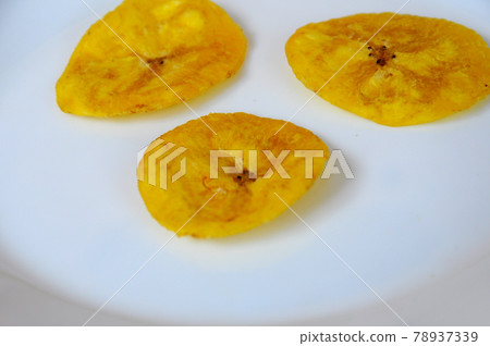 Dried and fried banana slices place on white plate isolated on wood texture background. This is local Malaysian traditional junk food call Kerepek Pisang. Dried and fried banana slices place on white plate isolated on wood texture background. This is local Malaysian traditional junk food call Kerepek Pisang. 78937339